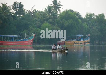 Zwei Männer, eine kleinere Kanu rudern, vorbei an großen bunten Fischerboote auf der West Coast Canal (National Wasserstraße Nr. 3), Kanjippadom, in der Nähe von Alappuzha (Alleppey), Kerala, Indien Stockfoto