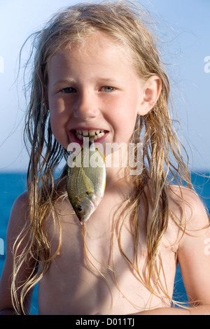 kleines Mädchen mit rohem Fisch im Mund Stockfoto