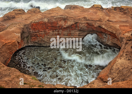 Wellen stürzen in die Flechten Wände des Teufels Punchbowl State Natural Area zentrale Küste Oregons und Lincoln County. Stockfoto