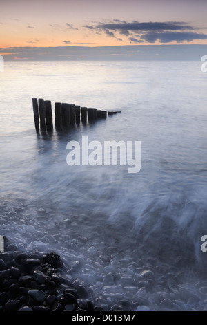 Flut waschen über Felsen und hölzernen Buhnen am Bossington Strand, Somerset, UK. Stockfoto