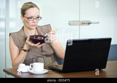 Das Business Office in ihrer Mitte 30 ist an ihrem Schreibtisch Müsli Essen. Stockfoto