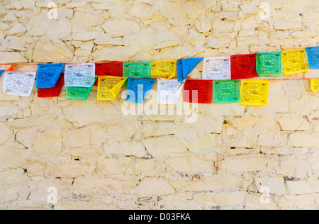 Buddhistische tibetische Gebetsfahnen gegen Steinmauer Stockfoto