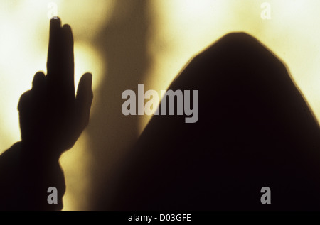 Schatten der vermummten Mönch oder Priester hielt seine Hand und Finger in Segen vor dem hellen Fensterlicht Stockfoto