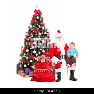 Weihnachtsmann mit Kind auf dem Schoß, posieren, einen Weihnachtsbaum im Hintergrund Stockfoto