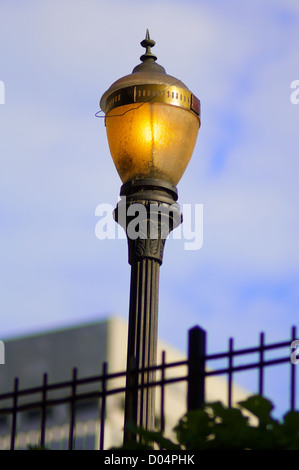 Alten Licht Post mit blauem Himmelshintergrund und schwarzen Zaun im Vordergrund. Stockfoto