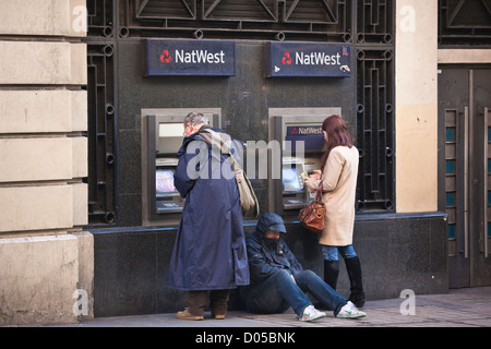 Menschen Sie ziehen Geld von einem Geldautomaten außerhalb NatWest Bank, während ein Mann betteln sitzt, Covent Garden, London, UK Stockfoto