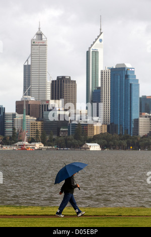 Ein Mann zu Fuß in den Regen halten einen Regenschirm mit Skyline einer Stadt im Hintergrund Stockfoto
