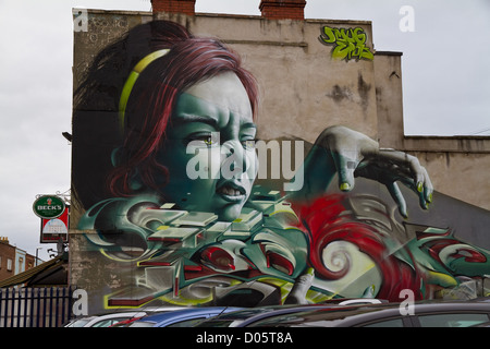 Graffiti von höhnischen das Gesicht einer Frau mit greifen Hand, grüne Augen und grün lackierten Fingernägel über einem Autohändler in Bristol Stockfoto