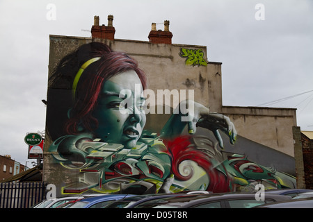 Graffiti von höhnischen das Gesicht einer Frau mit greifen Hand, grüne Augen und grün lackierten Fingernägel über einem Autohändler in Bristol Stockfoto