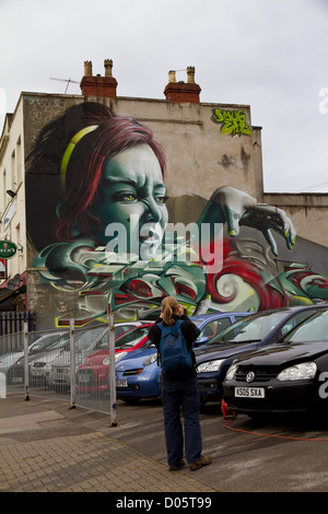 Graffiti von höhnischen das Gesicht einer Frau mit greifen Hand, grüne Augen und grün lackierten Fingernägel über einem Autohändler in Bristol Stockfoto