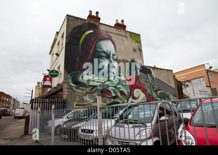 Graffiti von höhnischen das Gesicht einer Frau mit greifen Hand, grüne Augen und grün lackierten Fingernägel über einem Autohändler in Bristol Stockfoto