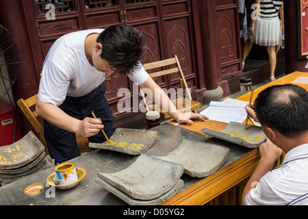Ein Mann schreibt ein Gebet auf einer Fliese Tempel Chenghuang Miao oder City God Temple in Yu Yuan Gardens Basar Shanghai, China Stockfoto