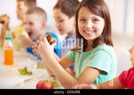 Gruppe von Mitschülern mit Mittagessen während der Pause mit Fokus auf lächelndes Mädchen mit sandwich Stockfoto