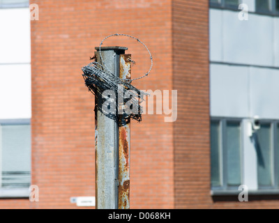 Stacheldraht aufgerollt auf einem Eisenpfahl vor ein Gebäude aus roten Backstein, Stadtlandschaft Stockfoto