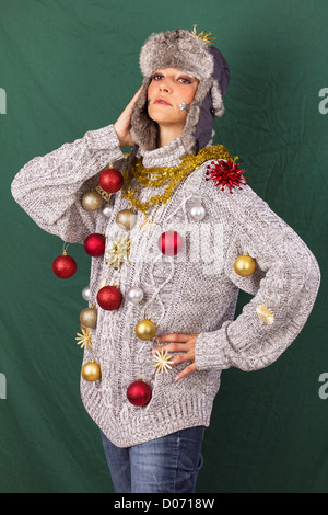 Schöne junge Frau im grauen Pullover posiert wie ein geschmückter Weihnachtsbaum, lustige Xmas Studio Aufnahme vor einem grünen Hintergrund Stockfoto