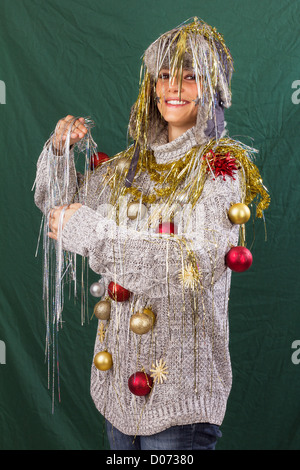 Schöne junge Frau freundlich lächelnd posiert wie ein geschmückter Weihnachtsbaum, lustige Xmas Studio Aufnahme vor einem grünen Hintergrund Stockfoto