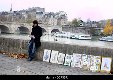 Ein Mann liest ein Buch, das Kunstwerk von der Seine in Paris Stand. Tour-Fluss-Boote vorbeiziehen im Hintergrund Stockfoto