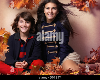 Führerschein und Fingerabdrücke bei MaximImages.com - ein lächelnder Junge und ein Mädchen im Teenageralter in trendigen Kleidern, die zusammen sitzen, umgeben von wunderschönen roten Herbstblättern Stockfoto