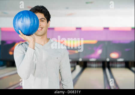 Junger Mann hält eine Bowling-Kugel in einer Bowlingbahn Stockfoto