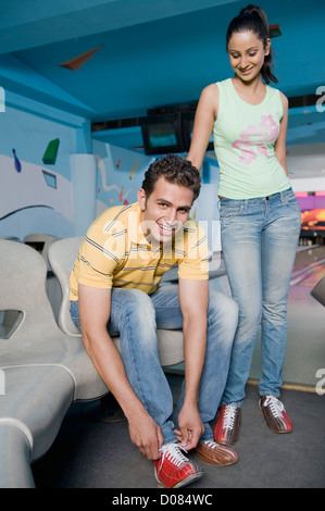 Porträt eines jungen Mannes mit seiner Freundin in einer Bowlingbahn hinter ihm steht seine Schnürsenkel zu binden Stockfoto