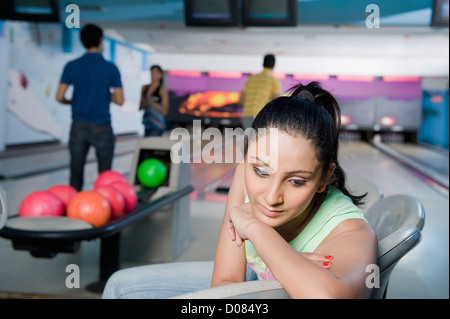 Junge Frau mit ihren Freunden im Hintergrund in einer Bowlingbahn denken Stockfoto