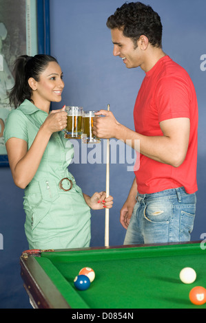 Junges Paar, toasten Bier Gläser im Poolraum Stockfoto