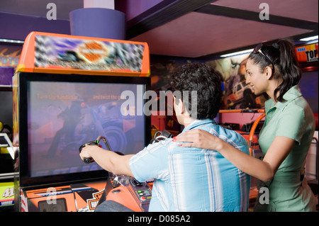 Junger Mann spielen Video-Spiel und eine junge Frau, die gerade sein Spiel in eine Spielhalle Stockfoto