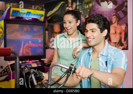 Junger Mann spielen Video-Spiel und eine junge Frau, die gerade sein Spiel in eine Spielhalle Stockfoto