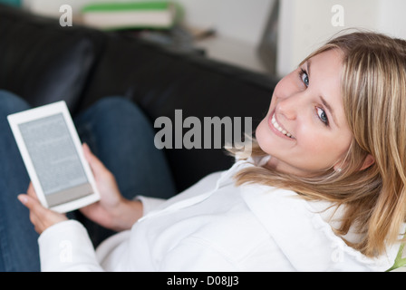 Junge schöne Frau sitzt auf einer Couch mit einem eBook Reader in ihren Händen Stockfoto