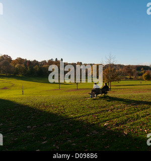 Herbstszene im Gadebridge Park, Hemel Hempstead, Hertfordshire, Großbritannien. 2 Personen auf einer Bank genießen die Landschaft. Stockfoto