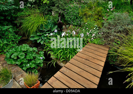 Freude, Garten, ein Becken mit Wasserpflanzen, Hosta, Iris und Dekoration mit einem Vogel aus Metall und kleine Brücke. Stockfoto