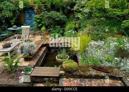 Lustgarten in der Normandie (Frankreich). Ein Becken mit Wasserpflanzen, eine Terrasse mit Gartenmöbeln. Stockfoto