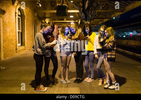 Eine Gruppe von sieben 14 15 jährigen Mädchen im Teenageralter Freunde zusammen außerhalb SMS Nachrichten auf ihren Mobiltelefonen bei Nacht UK Stockfoto