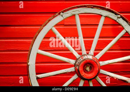 Alten verwitterten Waggon Rad an gemalte rote Wand gelehnt Stockfoto