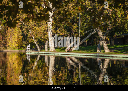 Ein Blick auf die Badestelle im Fluss in Bidwell Flusspark mit Reflexionen und ein Mann entspannend auf Parkbank in Chico CA. Stockfoto