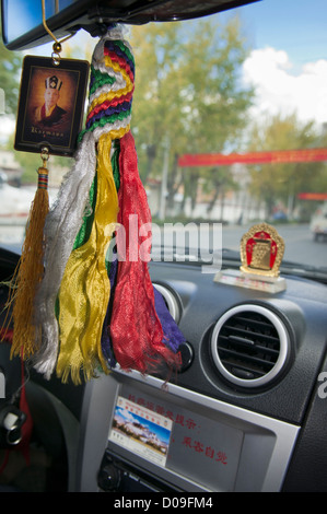 Bild der Mönch hängt von Taxi Driver-Spiegel während religiöse Andenken auf Armaturenbrett, Lhasa, Tibet sitzt Stockfoto