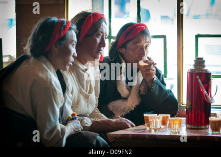 Ihre Haare geflochten und Sheap Haut Mäntel tragen, tibetische Hirten trinken Yak Buttertee im Straßencafé, Namtso, Tibet, China Stockfoto