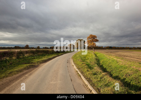 Gewitterwolken über eine englische Ackerland Landschaft mit einer wicklung ländlicher Highway und Bäumen Stockfoto