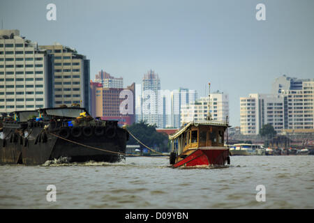 17. November 2012 - Bangkok, Thailand - Schlepper Lastkähne hochziehen Chao Phrya River in Bangkok. Bangkok war früher bekannt als das "Venedig des Ostens '' aufgrund der Anzahl der Wasserstraßen, die Kreuz und quer die Stadt gekreuzt. Nun die meisten der Wasserstraßen ausgefüllt aber Boote und Schiffe nach wie vor eine wichtige Rolle im täglichen Leben in Bangkok. Tausende von Menschen pendeln täglich auf dem Chao Phraya Express Boote und Schnellboote, die ply Khlong Saen Saeb oder Boote verwenden, um die Kanäle auf der Thonburi-Seite des Flusses zu erkunden. Boote werden verwendet, um die Rohstoffe durch die Stadt Tiefwasser-Häfen für Hol Stockfoto