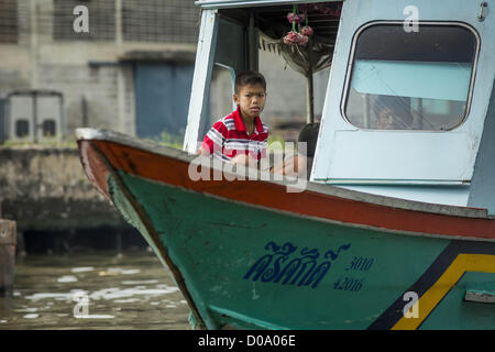 17. November 2012 sitzt im Steuerhaus von seiner Familie Boot an einem Kanal im Abschnitt Thonburi, Bangkok - Bangkok, Thailand - ein Junge. Bangkok war früher bekannt als das "Venedig des Ostens '' aufgrund der Anzahl der Wasserstraßen, die Kreuz und quer die Stadt gekreuzt. Nun die meisten der Wasserstraßen ausgefüllt aber Boote und Schiffe nach wie vor eine wichtige Rolle im täglichen Leben in Bangkok. Tausende von Menschen pendeln täglich auf dem Chao Phraya Express Boote und Schnellboote, die ply Khlong Saen Saeb oder Boote verwenden, um die Kanäle auf der Thonburi-Seite des Flusses zu erkunden. Boote werden verwendet, um Rohstoffe Thr schleppen Stockfoto