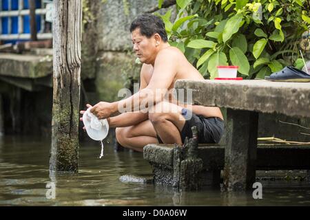 17. November 2012 - Bangkok, Thailand - ein Mann hat seine Gerichte in den Gewässern eines Khlong oder Kanal im Abschnitt "Thonburi" von Bangkok. Bangkok war früher bekannt als das "Venedig des Ostens '' aufgrund der Anzahl der Wasserstraßen, die Kreuz und quer die Stadt gekreuzt. Nun die meisten der Wasserstraßen ausgefüllt aber Boote und Schiffe nach wie vor eine wichtige Rolle im täglichen Leben in Bangkok. Tausende von Menschen pendeln täglich auf dem Chao Phraya Express Boote und Schnellboote, die ply Khlong Saen Saeb oder Boote verwenden, um die Kanäle auf der Thonburi-Seite des Flusses zu erkunden. Boote werden verwendet, um Rohstoffe Throu schleppen Stockfoto