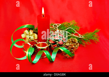 Brennende Kerze, Christbaumschmuck in Form einer Kugel, eine Hand-Glocke mit einem Bogen, eine Trommel, Kegel gegen rote Seide rot Stockfoto