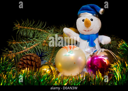Gekleidet in eine blaue Mütze und Schal Schneemann Weihnachten Spielzeug, glänzend grünen Lametta und Weihnachtsbäume auf einem schwarzen staatlich umgeben Stockfoto