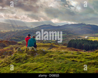 junges Paar, Mann sitzt auf Felsen, Weibchen sitzt auf seinem Knie schauen über Tal, Herbst, bergigen Hintergrund, stürmische Himmel Stockfoto
