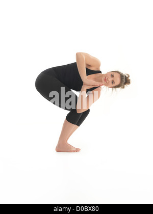 junge Frau zeigt schwierige Yoga-Pose, gekleidet in Balc, auf weißem Hintergrund Stockfoto
