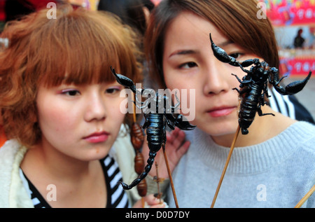 Zwei Frauen schauen einem frittierten Skorpion auf einen Stock an der Anhui Wuhu Phoenix Gourmetfestival in AnHui. Über 200 ausgefallene Snacks von Stockfoto