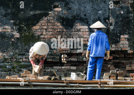 HUE, Vietnam – Arbeiter renovieren eine beschädigte Mauer in der Kaiserstadt in Hue, Vietnam. Der Komplex ist ein selbstgeschlossener und befestigter Palast und umfasst die lila Verbotene Stadt, die das innere Heiligtum des kaiserlichen Haushalts war, sowie Tempel, Höfe, Gärten und andere Gebäude. Ein großer Teil der Kaiserlichen Stadt wurde während des Vietnamkrieges beschädigt oder zerstört. Sie ist heute zum UNESCO-Weltkulturerbe ernannt. Stockfoto