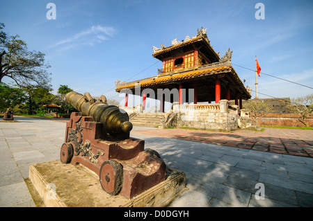 HUE, Vietnam – Eine Kanone und eine Pagode vor dem Graben in der Kaiserstadt in Hue, Vietnam. Der Komplex ist ein selbstgeschlossener und befestigter Palast und umfasst die lila Verbotene Stadt, die das innere Heiligtum des kaiserlichen Haushalts war, sowie Tempel, Höfe, Gärten und andere Gebäude. Ein großer Teil der Kaiserlichen Stadt wurde während des Vietnamkrieges beschädigt oder zerstört. Sie ist heute zum UNESCO-Weltkulturerbe ernannt. Stockfoto