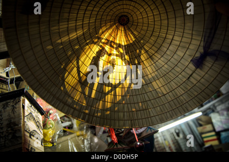 Vietnamesischer konischer Hut romantisches Paar Design Hue Vietnam // HUE, Vietnam — Ein dekorierter Bambushut mit romantischem Paar Design wird auf dem Cho Dong Ba, dem wichtigsten Stadtmarkt in Hue, ausgestellt. Der traditionelle vietnamesische konische Hut, der lokal als nón lá bekannt ist, zeigt komplizierte künstlerische Details, die typisch für regionales Kunsthandwerk sind. Cho Dong Ba ist der wichtigste Marktplatz von Hue und bietet Einwohnern und Besuchern lokale Waren und traditionelles Kunsthandwerk an. Der Markt befindet sich in der ehemaligen kaiserlichen Hauptstadt Vietnams in der zentralen Provinz Thua Thien-Hue. Hue ist weithin anerkannt f Stockfoto