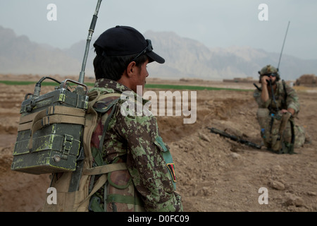 Ein Soldat der Afghan National Army Uhren ein US-Soldat sein Radio während einer afghanischen Kraft führte Sicherheitspatrouille 30. Oktober 2012 in Khak-E-Safed, Farah Provinz, Afghanistan zu verwenden. Afghanischen Streitkräfte haben die Führung in Sicherheits-Operationen mit Koalitionstruppen als Mentoren statt. Stockfoto